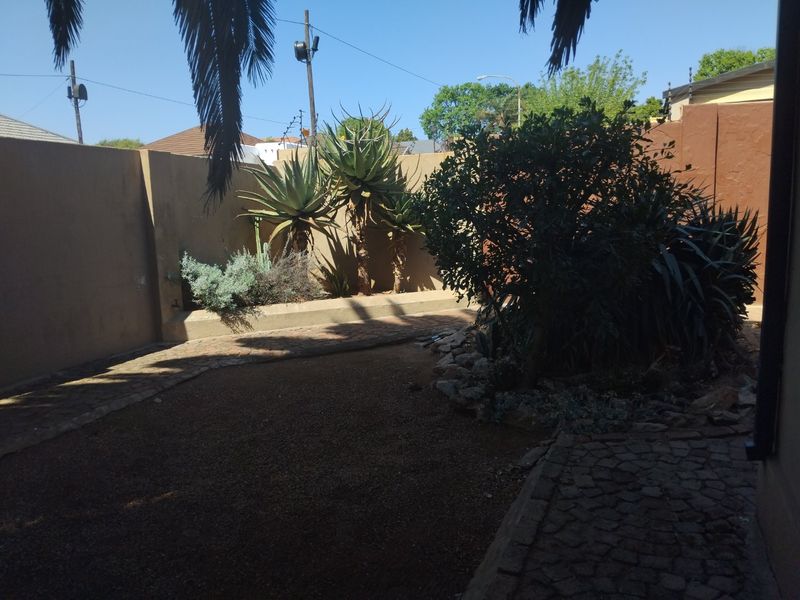 A private rear garden area featuring a paved walkway, raised garden beds with established succulents, and high boundary walls for privacy.