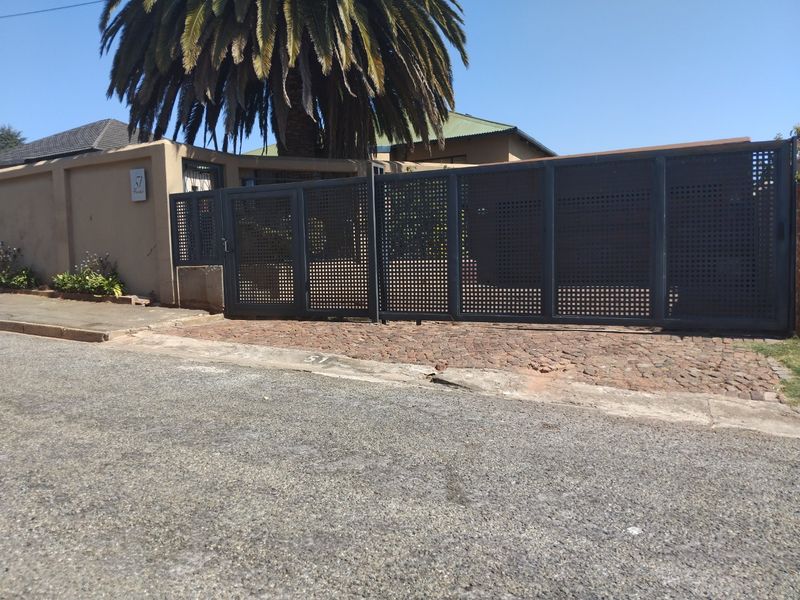 Front view of the property featuring a modern dark metal security gate, perimeter wall, and cobblestone driveway entrance.