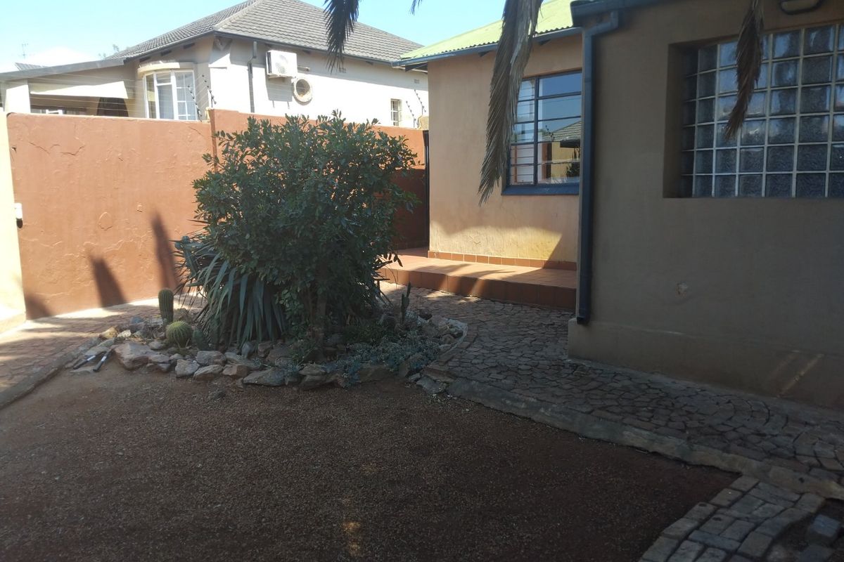 Rear exterior view of the property featuring a tiled patio area, cobblestone paving, and a private garden space enclosed by a boundary wall.