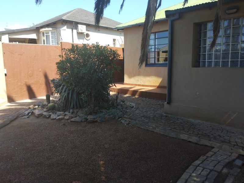 Rear exterior view of the property featuring a tiled patio area, cobblestone paving, and a private garden space enclosed by a boundary wall.