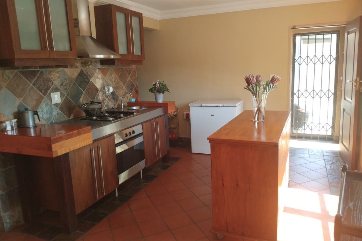 A functional kitchen featuring wooden cabinetry, a stainless steel extractor fan, built-in oven, gas hob, and durable terracotta floor tiles with a rear security door.