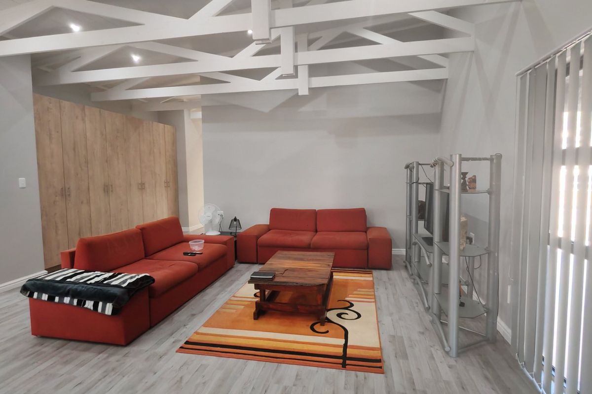 Spacious living area featuring high ceilings with exposed white timber trusses, modern laminate flooring, and extensive built-in storage cabinetry.