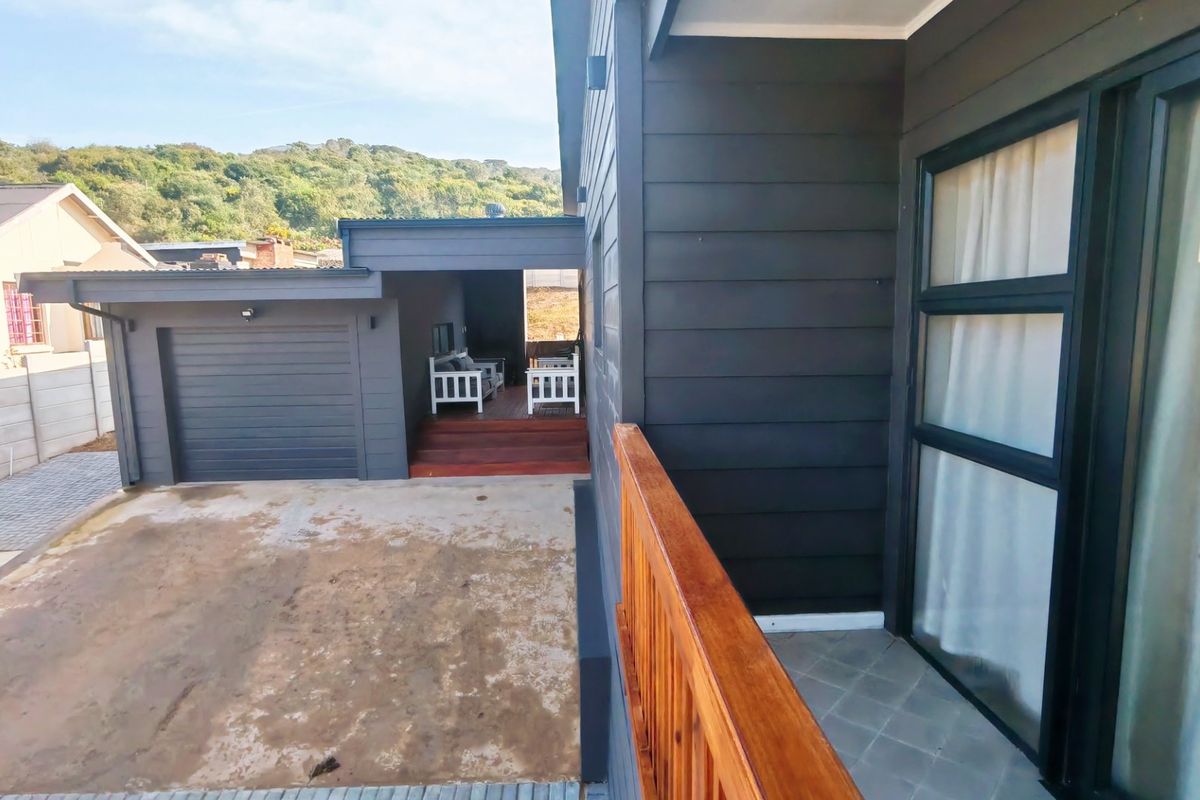 Rear exterior view showing a garage, timber deck area, and modern dark horizontal cladding with a wooden balustrade.