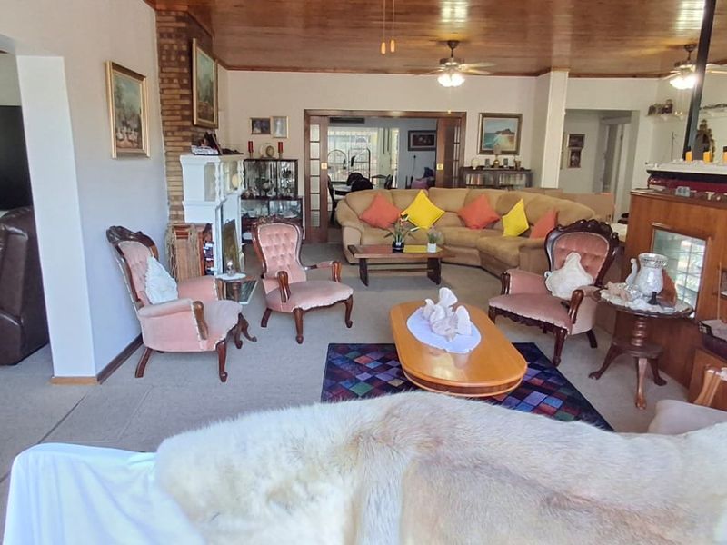 Spacious open-plan living area featuring a brick fireplace, timber-clad ceilings, and ceiling fans, providing a warm and traditional atmosphere.