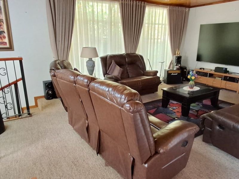 A spacious living room featuring carpeted flooring, a timber ceiling, and a decorative wrought iron staircase railing.