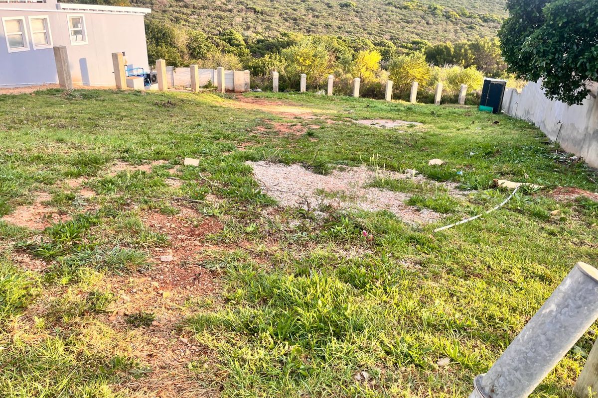 A view of a vacant residential plot featuring a grass lawn, perimeter boundary wall, and concrete fence posts.