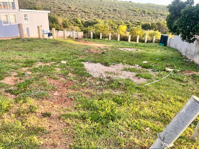 A view of a vacant residential plot featuring a grass lawn, perimeter boundary wall, and concrete fence posts.