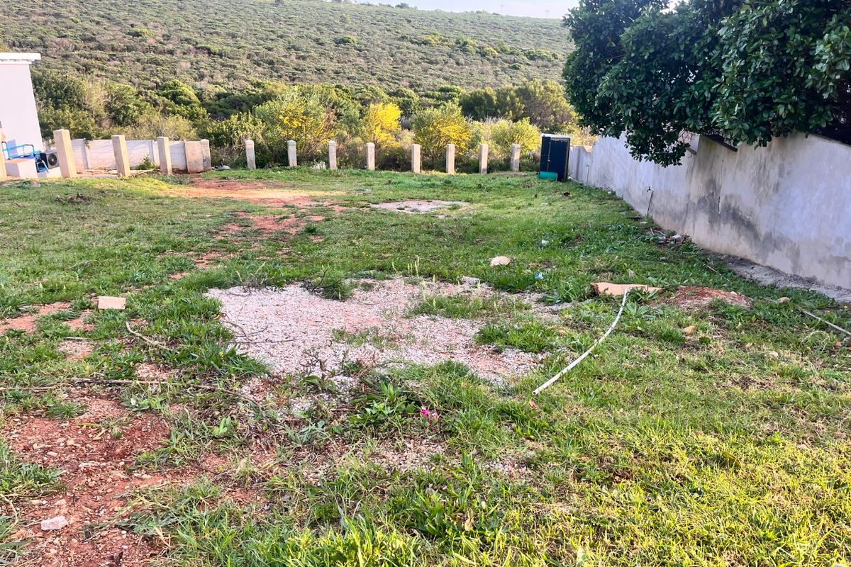 A vacant residential plot featuring a boundary wall, concrete fence posts, and natural landscape with views of the surrounding hillside.