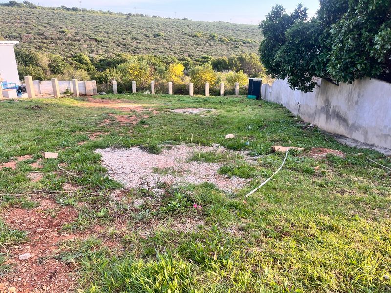 A vacant residential plot featuring a boundary wall, concrete fence posts, and natural landscape with views of the surrounding hillside.