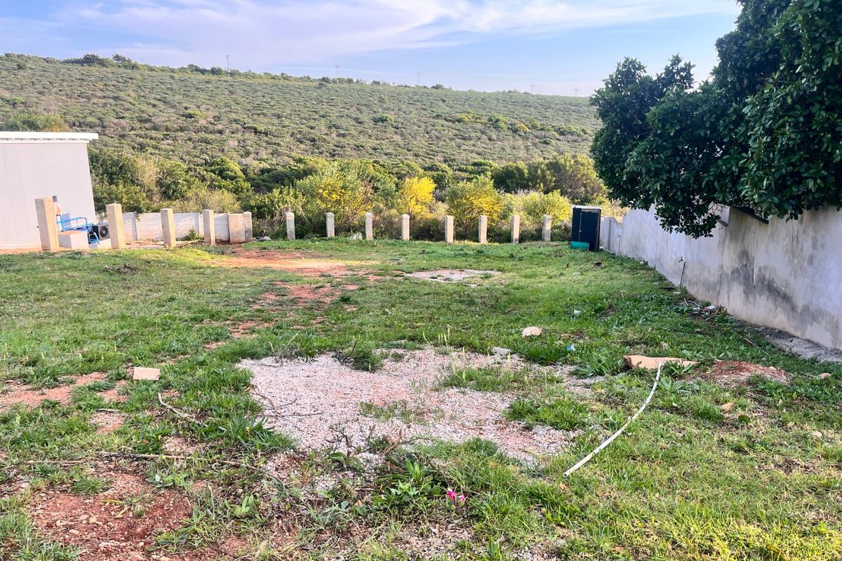A vacant residential plot featuring a boundary wall, concrete fence posts, and natural landscape with views of the surrounding hillside.