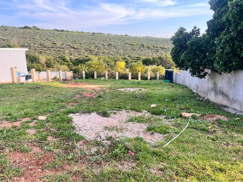 A vacant residential plot featuring a boundary wall, concrete fence posts, and natural landscape with views of the surrounding hillside.