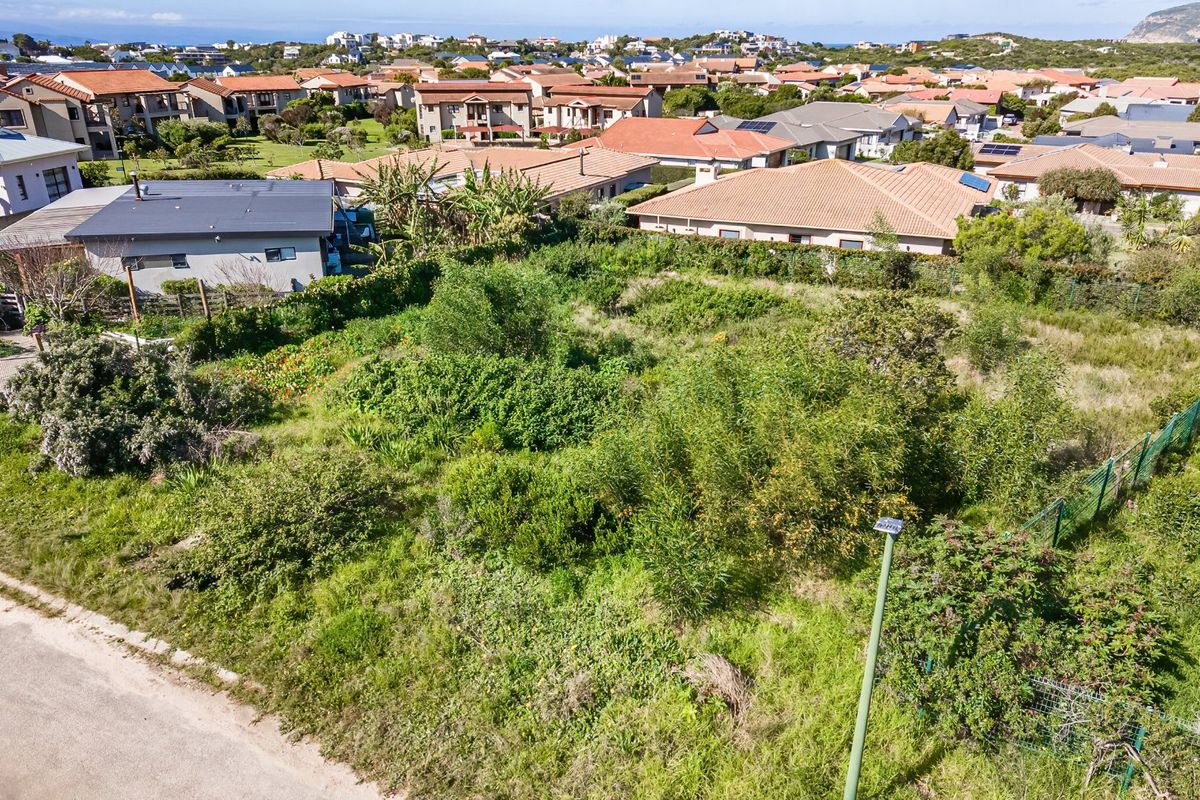 An aerial view of a vacant residential plot featuring natural vegetation and perimeter fencing, situated within an established suburban neighborhood.
