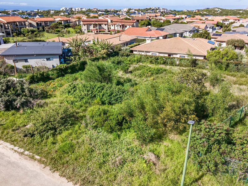 An aerial view of a vacant residential plot featuring natural vegetation and perimeter fencing, situated within an established suburban neighborhood.