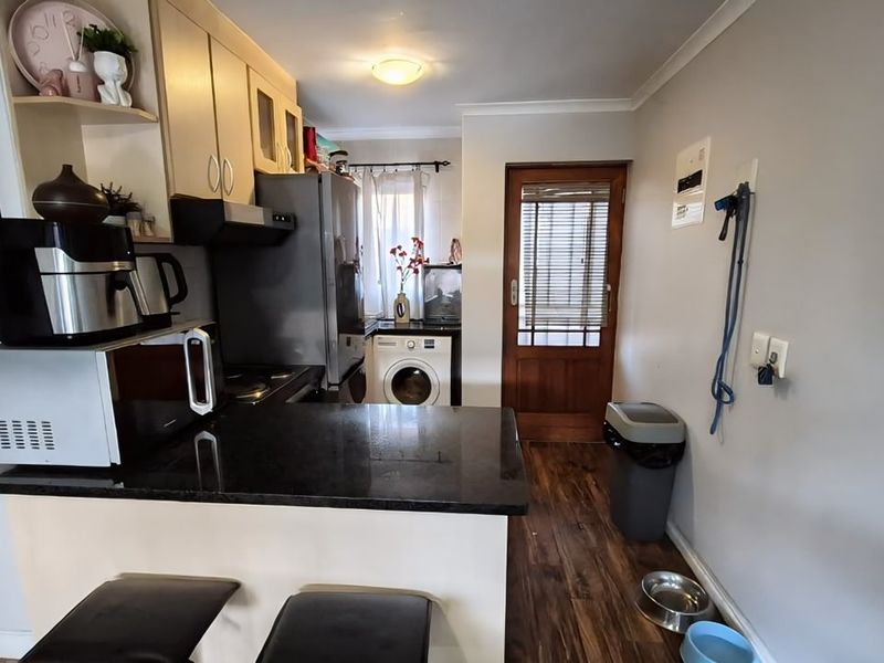 Compact kitchen featuring granite countertops, built-in cabinetry, and integrated appliances, with direct access to an exterior door and laminate flooring throughout.