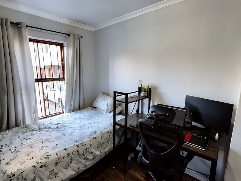 A functional bedroom featuring hardwood flooring, coving, and a window fitted with security bars.