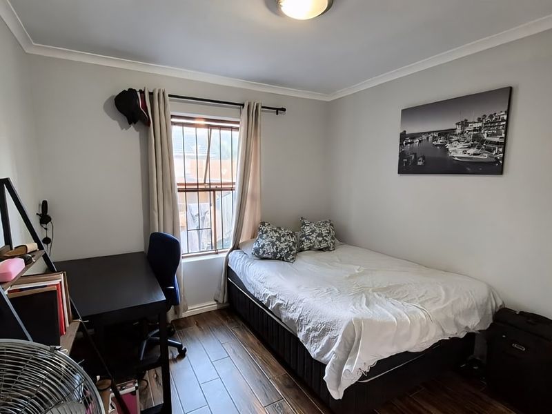 A compact bedroom featuring wood-look tile flooring, a window with security bars, and neutral wall finishes.