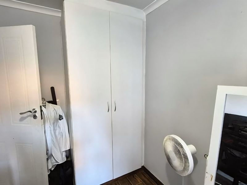 A bedroom featuring a white built-in wardrobe, coving, and timber-look flooring.