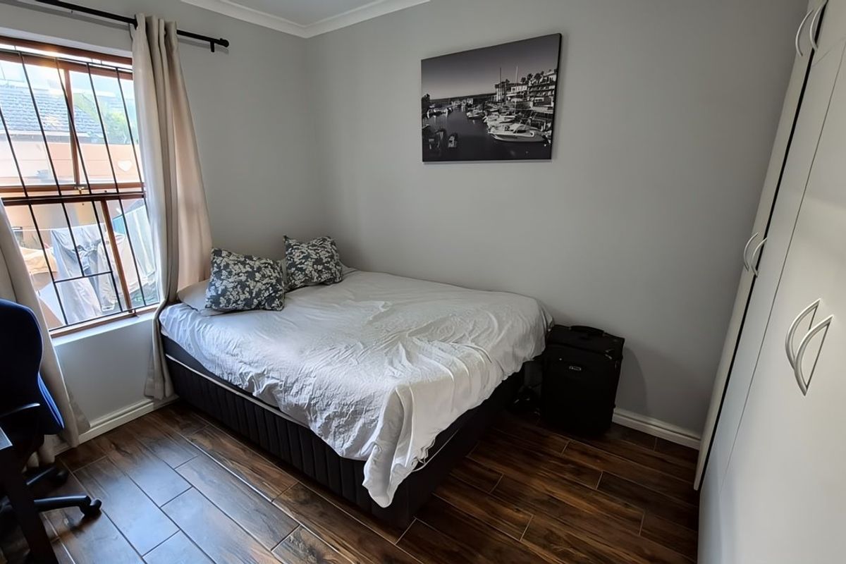 A well-maintained bedroom featuring durable laminate flooring, a built-in wardrobe, and a window fitted with security bars for added peace of mind.