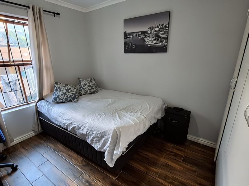 A well-maintained bedroom featuring durable laminate flooring, a built-in wardrobe, and a window fitted with security bars for added peace of mind.