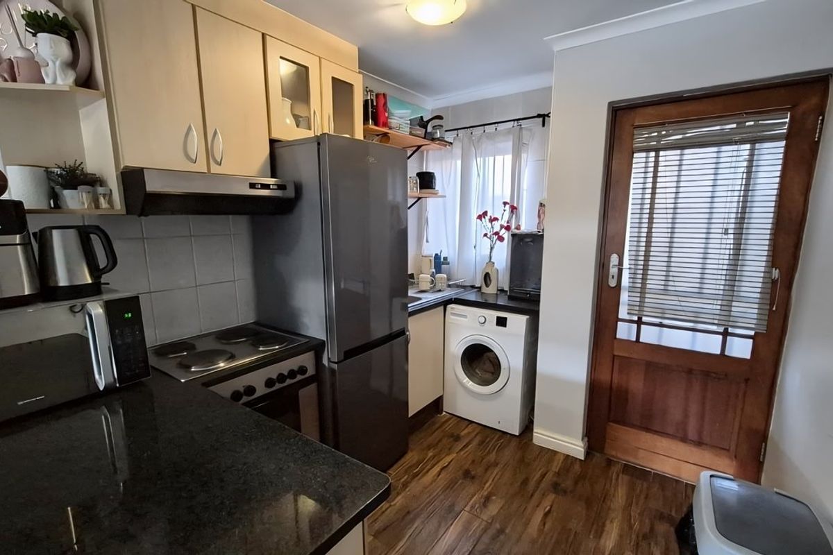 Compact kitchen featuring built-in cabinetry, granite countertops, electric hob, oven, and integrated laundry space with direct access to an exterior timber door.