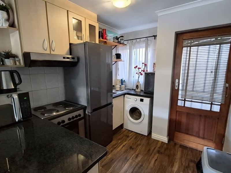 Compact kitchen featuring built-in cabinetry, granite countertops, electric hob, oven, and integrated laundry space with direct access to an exterior timber door.