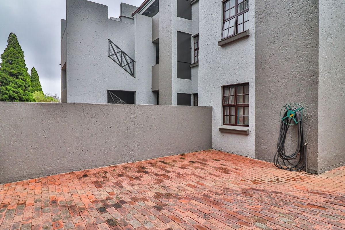 A private rear courtyard area featuring brick paving, a solid boundary wall, and access to the apartment building's exterior staircase and windows.