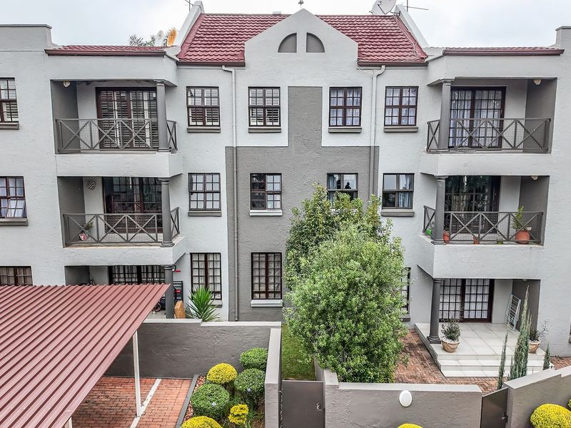 Rear elevation of a multi-story apartment complex featuring private balconies, a paved courtyard area, and a covered carport.