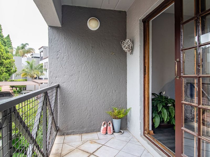 A compact balcony featuring tiled flooring, a metal mesh railing, and a sliding glass door providing access to the interior.