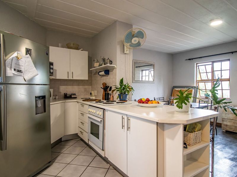 A functional kitchen featuring white cabinetry, built-in oven and hob, tiled flooring, and a breakfast counter, offering a practical layout for daily meal preparation.