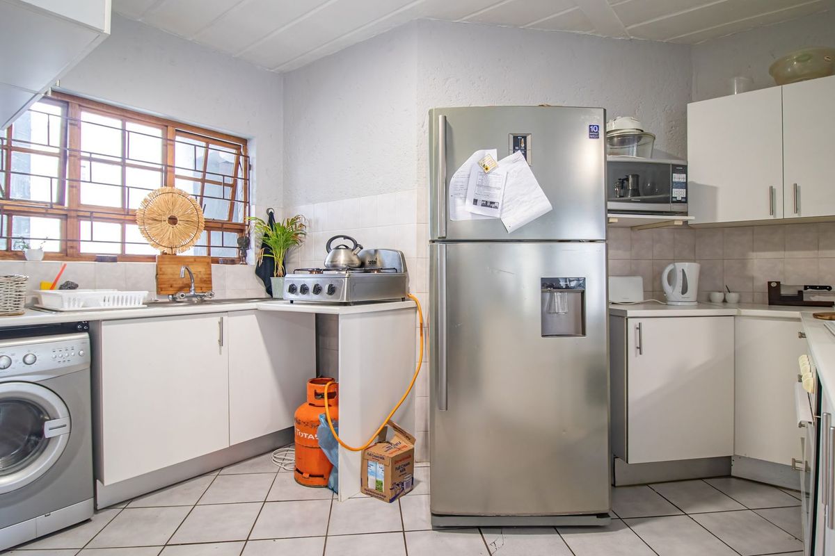 A functional kitchen featuring white cabinetry, tiled flooring, a tiled backsplash, and integrated microwave, with a window fitted with security bars.