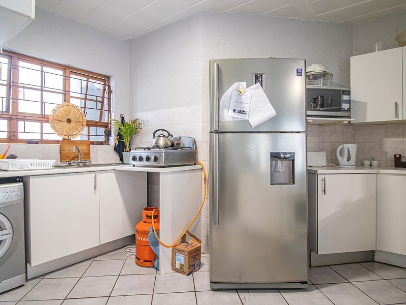 A functional kitchen featuring white cabinetry, tiled flooring, a tiled backsplash, and integrated microwave, with a window fitted with security bars.