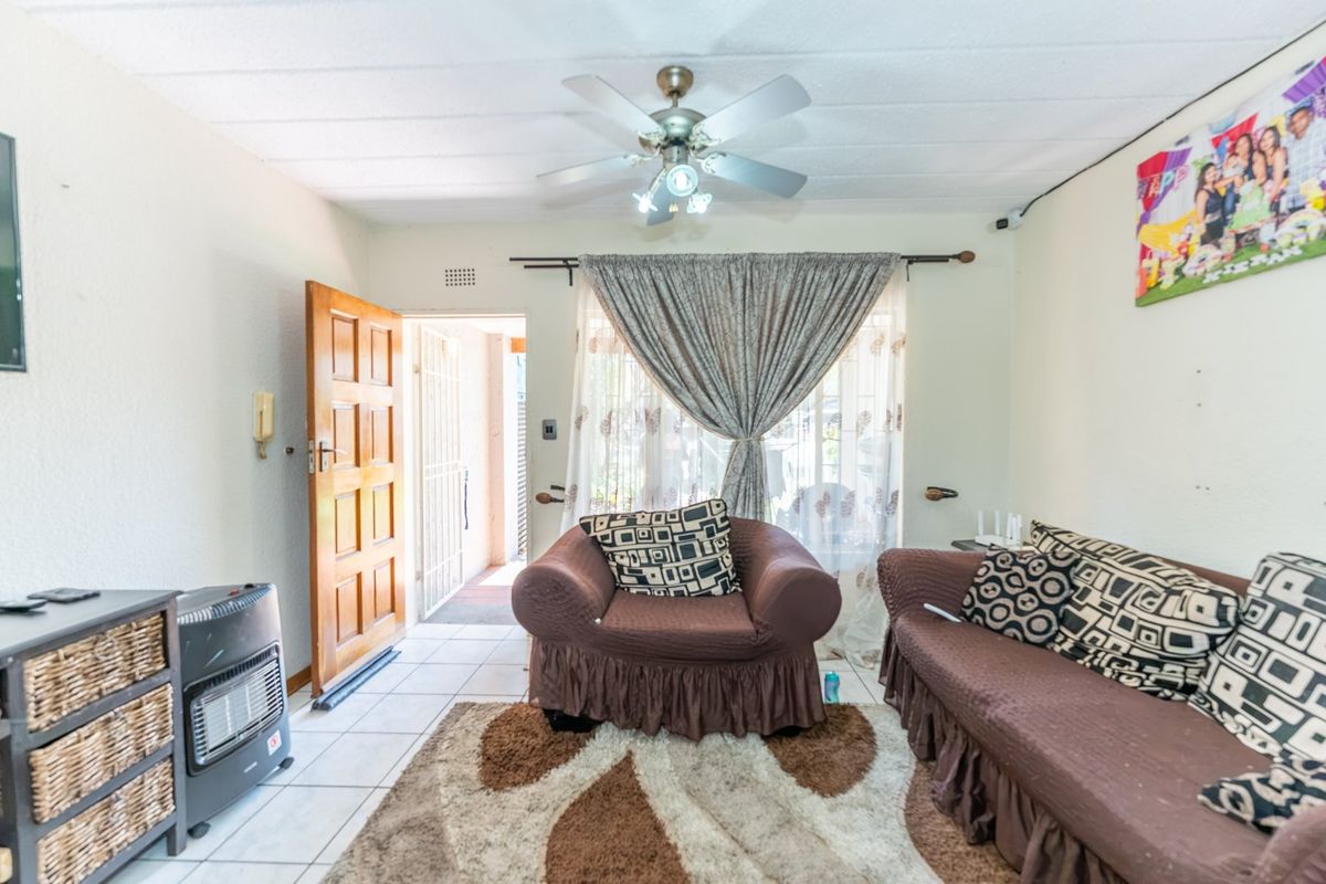 A living room featuring tiled flooring, a ceiling fan, and direct access to an outdoor area through a timber door with a security gate.