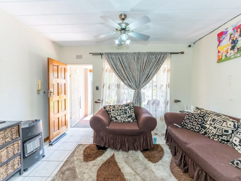 A living room featuring tiled flooring, a ceiling fan, and direct access to an outdoor area through a timber door with a security gate.