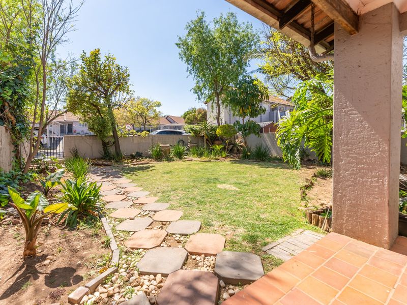 A private rear garden featuring a lawn, established trees, and a stone pathway, viewed from a covered tiled patio area.