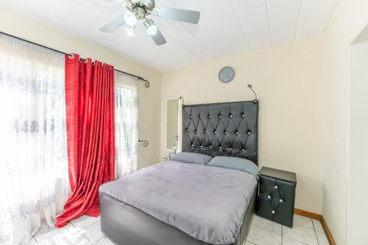 A bedroom featuring tiled flooring, a ceiling fan, and a large window with curtains.