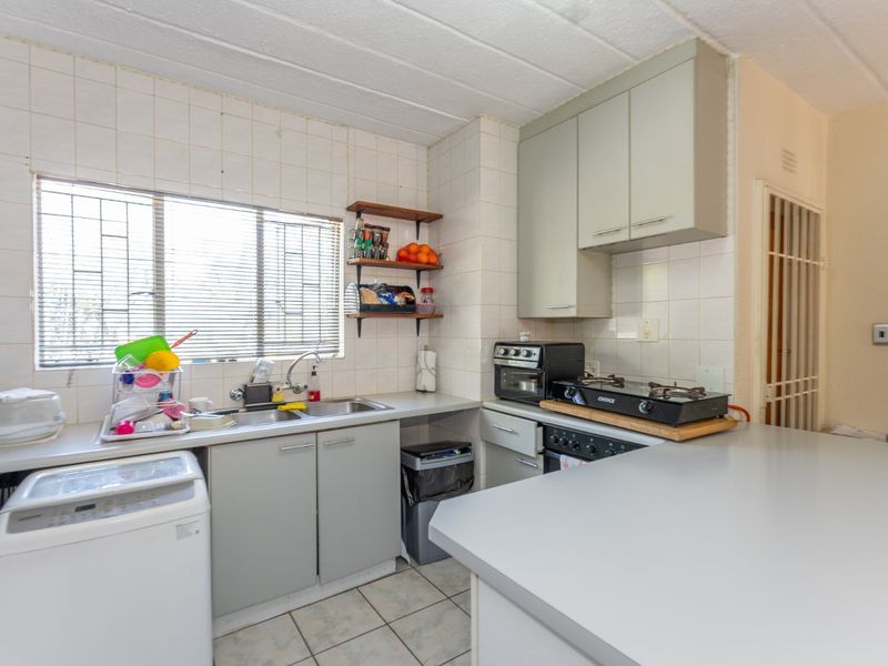 A functional kitchen featuring built-in cabinetry, a double sink, tiled backsplash, and a breakfast counter, with security gate access.
