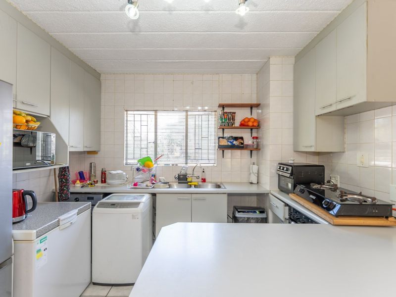 A functional kitchen featuring built-in cabinetry, a double sink, tiled backsplash, and ample counter space with integrated lighting.