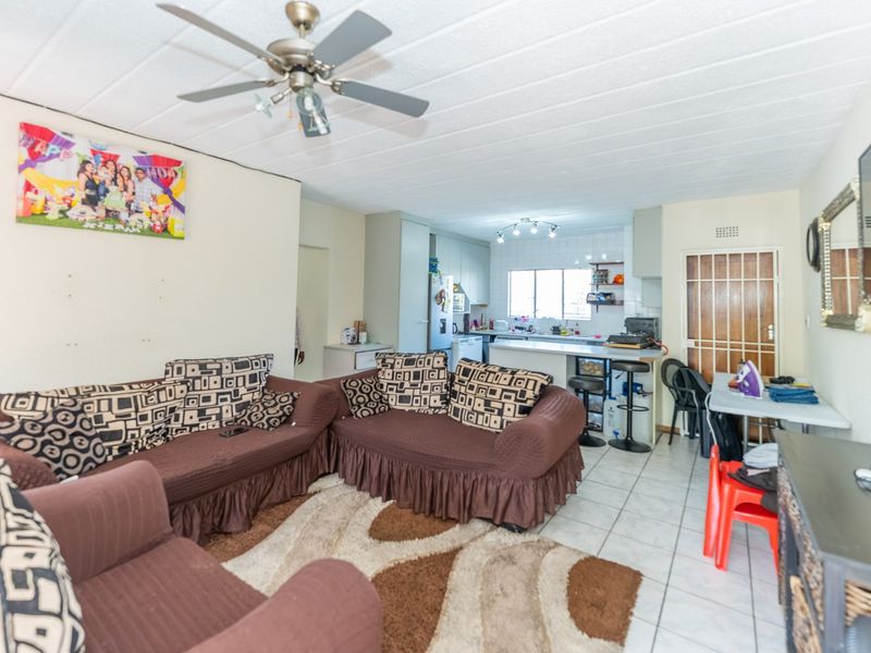 Open-plan living and kitchen area featuring tiled flooring, a ceiling fan, and functional kitchen cabinetry with a breakfast counter.