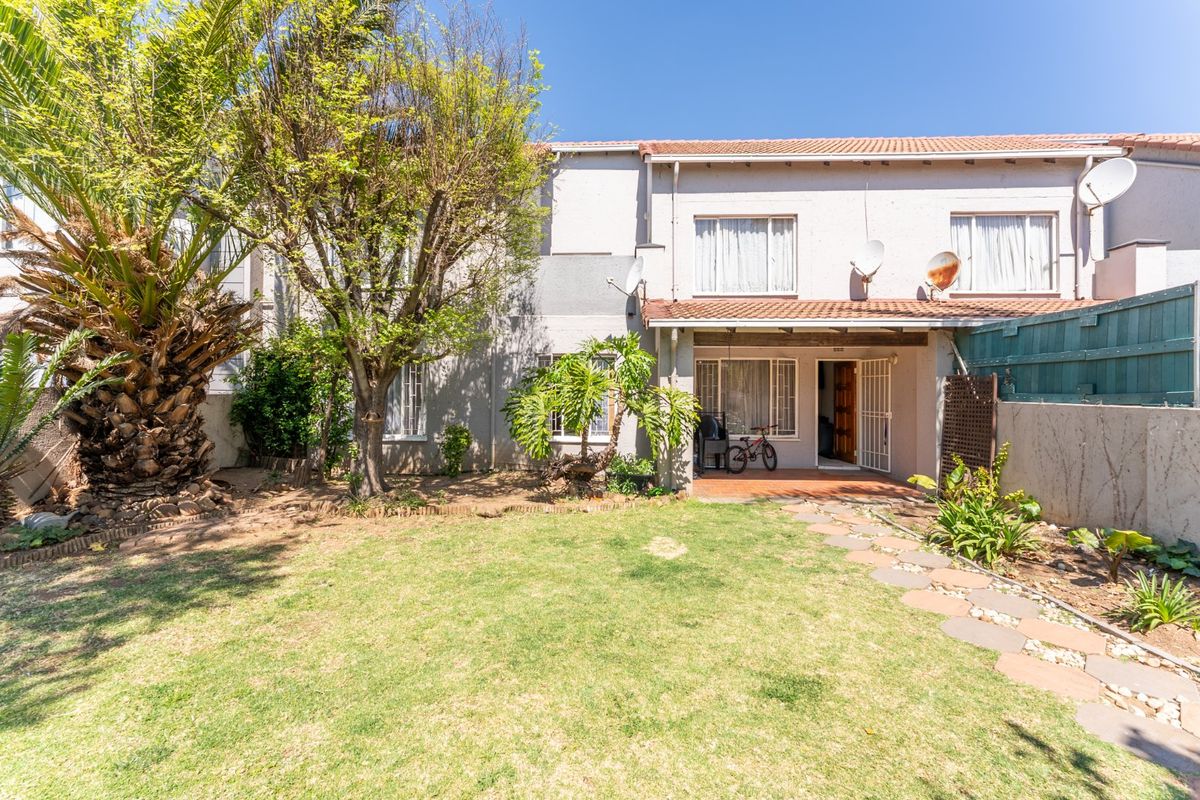 Rear view of the townhouse featuring a private garden, a covered patio area, and a paved walkway leading to the entrance.
