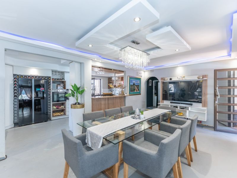 Spacious open-plan dining and living area featuring a modern recessed ceiling with ambient lighting, a crystal chandelier, and a built-in media unit.