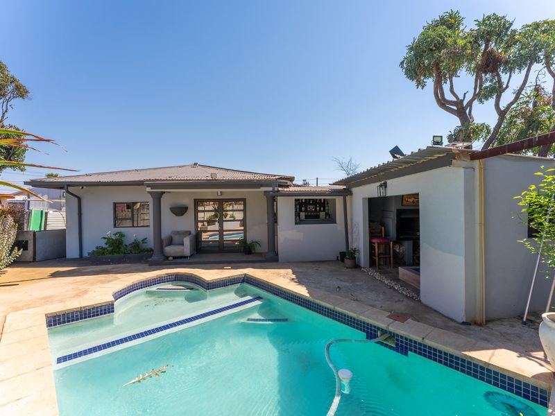 Rear outdoor entertainment area featuring a swimming pool, paved patio, and a built-in braai area under a covered structure.