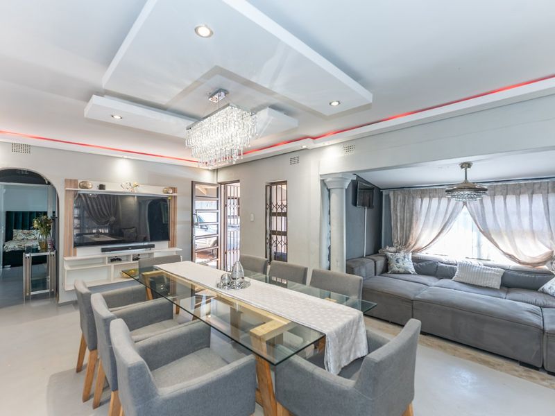Spacious open-plan living and dining area featuring a modern recessed ceiling with ambient lighting, a crystal chandelier, and a built-in media unit.