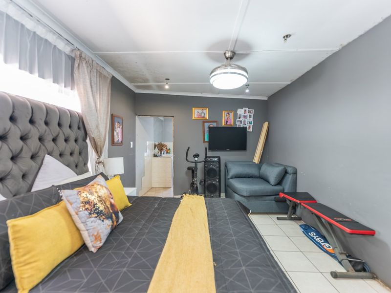 A bedroom featuring tiled flooring and a ceiling fan, showing visible signs of water damage and wear on the ceiling.