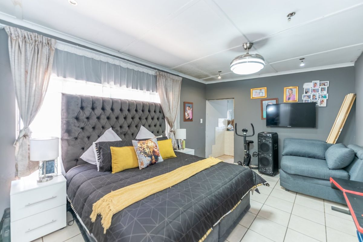 A bedroom featuring tiled flooring and a ceiling fan, with an adjacent doorway leading to an en-suite area.