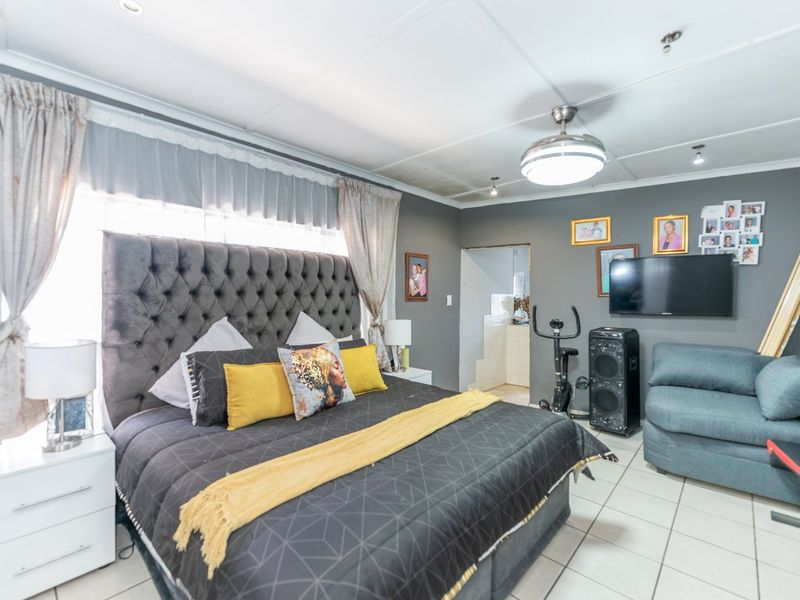 A bedroom featuring tiled flooring and a ceiling fan, with an adjacent doorway leading to an en-suite area.