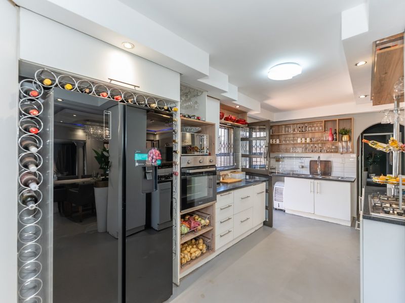 Modern kitchen featuring white cabinetry, built-in oven and microwave, stainless steel sink, and integrated wine storage with ample open shelving and recessed lighting.