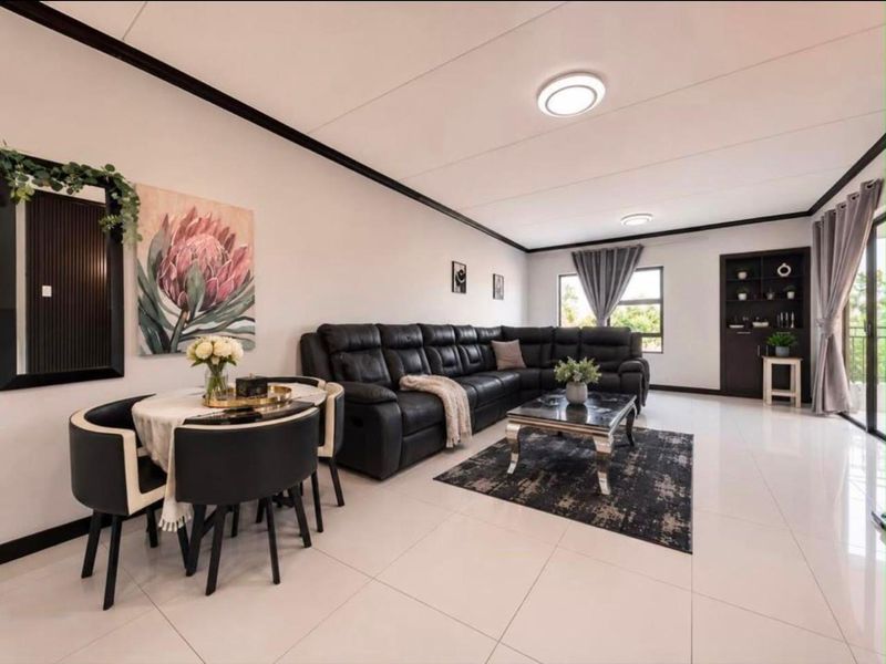 Spacious open-plan living and dining area featuring polished tile flooring, modern recessed lighting, and a built-in shelving unit with access to a balcony.