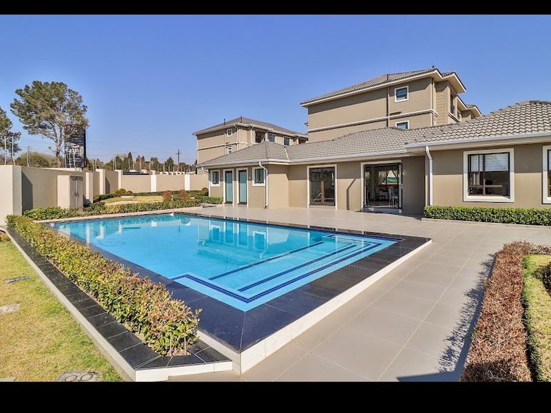 A well-maintained outdoor pool area featuring a tiled deck, clear swimming pool, and landscaped garden surroundings, set against the apartment building exterior.
