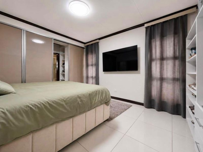 A well-maintained bedroom featuring large built-in sliding door wardrobes, tiled flooring, and a dedicated built-in shelving unit for storage.