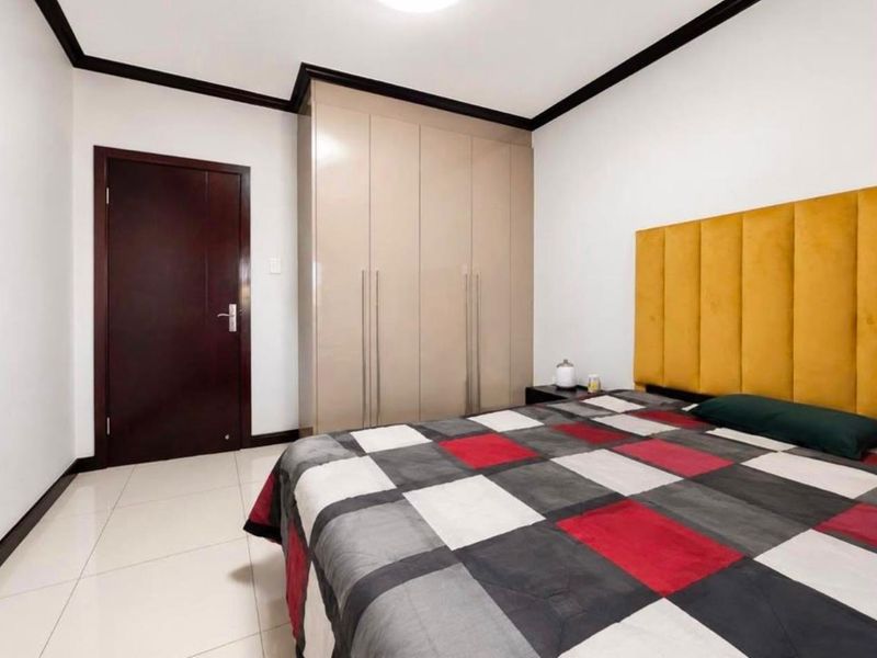 A well-maintained bedroom featuring neutral tiled flooring, dark wood trim, and integrated floor-to-ceiling built-in cupboards.